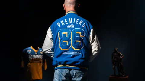 A fan in a 1986 Premiers varsity jacket beside a framed Eels jersey