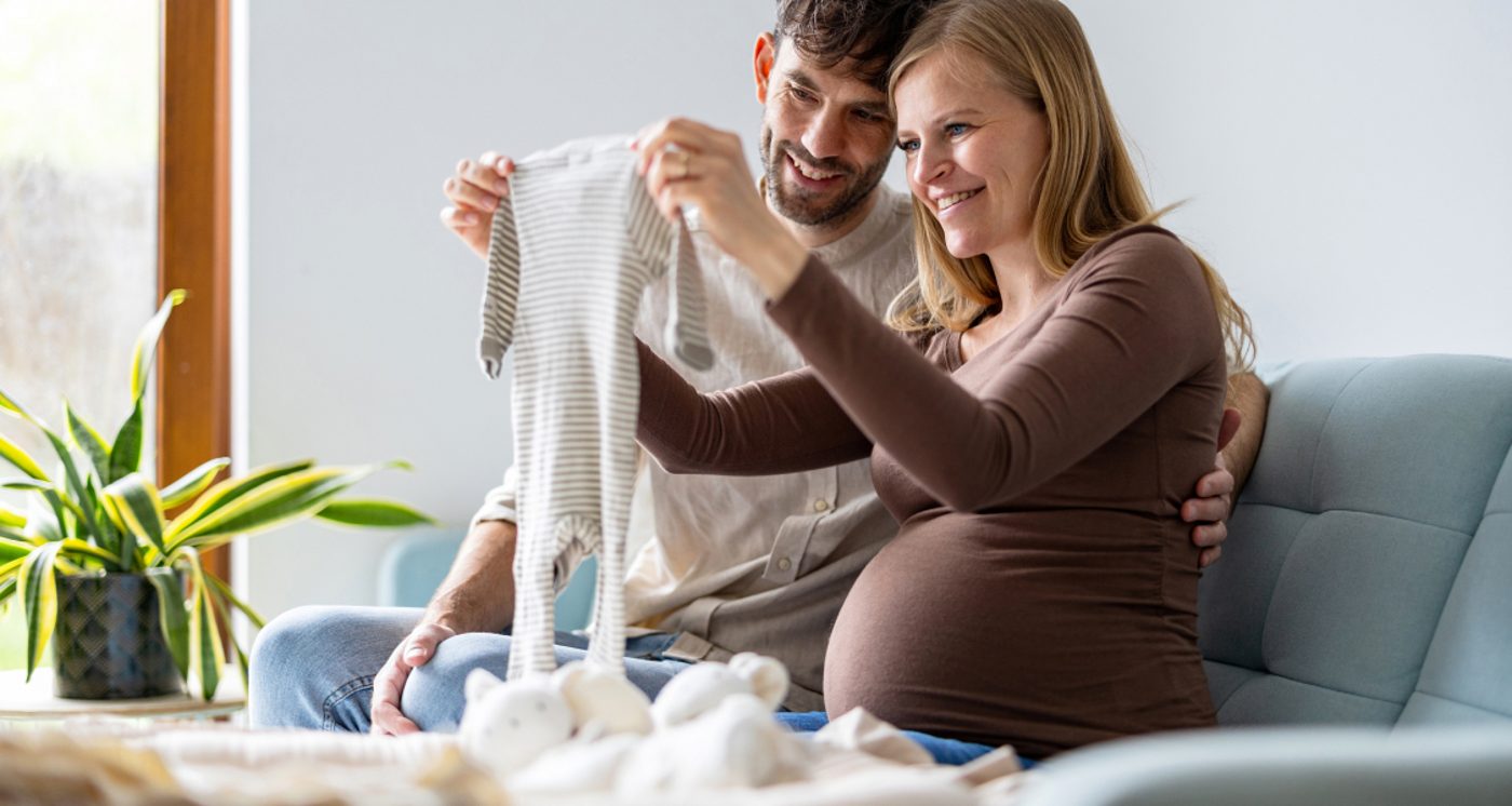 Expectant parents holding up a baby onesie together at home